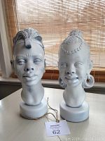 Pair of bisque busts on a table with a tag showing lot number 62, female on right and male on left