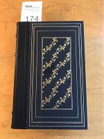 Front cover of the book showing dark leather cover with gold floral vine pattern and borders.