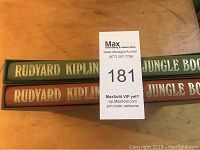 Two volumes of Rudyard Kipling's The Jungle Book in original slipcases with gilt tooled covers on a wooden surface.