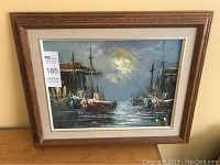 Framed oil painting showing entire artwork and frame, scene of boats in harbor at sunset or dusk, warm light reflecting on water.