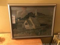 Full frontal view of framed painting showing church landscape scene and silver metal frame
