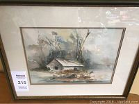 Framed landscape watercolour showing a small barn with trees in background, labeled with auction lot sticker.