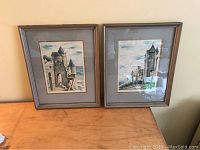 Two vintage colored etchings of Carcassonne displayed side-by-side on a wooden surface in matching gray mats and frames.