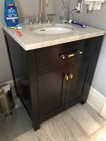 Front angle showing dark wood cabinet, recessed panel doors, chrome handles, marble top and sink