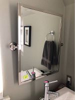 Front view of hinged wall mirror mounted above sink showing full frame and reflection
