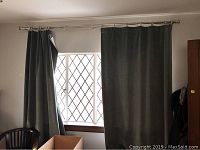 Two green velvet drapery panels hung on silver-tone metal rod above diamond-pane window