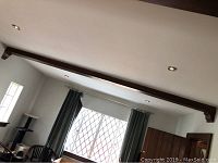 Full view of the decorative wooden ceiling beam installed on the ceiling spanning between walls with dark stain and smooth surface finish.