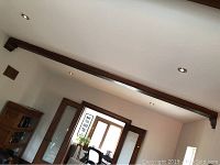 Long view of the dark stained wooden decorative ceiling beam installed horizontally on a white ceiling, showing overall condition and length