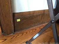 Photo of single section of oak baseboard trim installed along wall and floor with wood grain and trim profile visible.