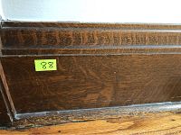 Close-up photo of oak baseboard corner showing dark stained wood with visible grain and molding detail.