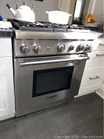 Front view of stainless steel range installed under countertop with kettle and pot on burners