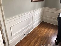 Corner view of white painted wainscoting on wall above hardwood floor