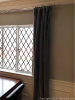 Gray drapery panel hung on polished metal rod above window