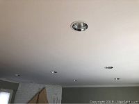 View of several round silver-trimmed pot lights recessed in white ceiling, showing installation and number.