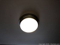 Ceiling light turned on showing bright white illumination with frosted glass diffuser and metal rim attached to ceiling.