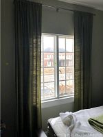 Window with closed green drapery panels hung on a metal curtain rod