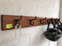 Full length view of the wooden coat rack mounted on a textured wall, showing six black metal hooks and some hanging items.