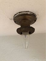Close-up photo of antique metal ceiling light fixture with flame-shaped bulb installed, showing decorative embossed metal ring and mounting plate.