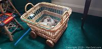 Rolling wicker table with glass top and leaf pumpkins inside, on green carpet.