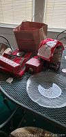 Overview of Christmas decorations on patio table including glass plate, Lenox dip bowl and spreader, holiday hand towels, gift bag, and other linens.