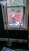 Brass-colored floor lamp with frosted glass shade near window showing vertical height and base