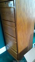 Side view of wood file cabinet showing four drawers and natural wood grain finish.