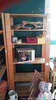 Frontal and angled view of six-shelf wooden shelving unit, placed against a dark wall with various items on shelves for scale.