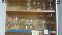 Shelf with 16 total Irish crystal glasses: 8 smaller cordial glasses on top left, and 8 larger stemware glasses on bottom.