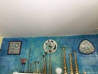 Four decorative plates hung on a blue wall along with brass candle holders and a lamp.