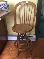 Front view of the vintage wooden drafting chair showing curved back with vertical spindles, round seat, metal swivel base, and footrest.
