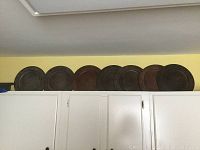 Wide angle photo showing eight metal plates lined up on top of cabinets. Plates vary in patina, colors ranging from dark brown to rusty and greenish tones.