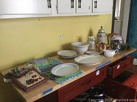 Full view of kitchen items placed on countertop, includes linens, plates, pitchers, mixing bowls, biscotti jar, and tureen