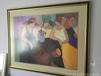 Framed wall art print showing colorful modern scene with three women at table, framed in gold and black with double mat.