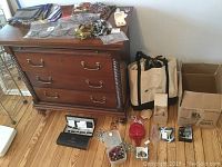 Wide view of chest with scarves on top and assorted jewelry, perfume, bags and boxes on floor beside it