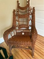 Front view of the tall back wicker chair showing woven seat, ornate back and armrest detailing with rocking rocker base.