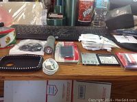 Photo showing black phone case with decorative studs, white charger cable, small flashlight, wired black earphones, assorted battery packs, and other small sealed accessories on a desk