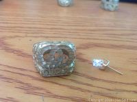 Men's ring with Gucci logo and wide band next to single stud earring with loose stone on a wooden surface.