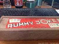 Top view of the rectangular wooden box with a vintage Rummy Joke label in red color and number graphics.