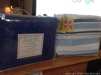 Two items: one deep blue embossed sheet set and one striped futon cover in packaging, shown on a wooden surface.