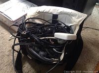 Close-up photo of tangled black power cords, USB cords, and cables inside a light fabric tote bag.