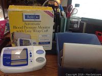 Full shot of the ReliOn blood pressure monitor, easy wrap cuff, and original yellow box on a desk.