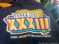Close-up of embroidered Super Bowl XXXIII logo with date Sunday January 31, 1999 and location Miami, Florida on jacket front.
