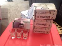 Photo showing stacked original boxes of bicchieri glasses and three sample glasses on a red table.