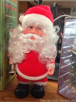 Vintage walking Santa Claus toy dressed in red, white beard and black boots holding a bell on a wooden surface.