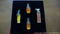 Four miniature Givenchy perfume bottles with amber contents displayed on a black velvet-lined tray.