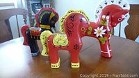 Photo showing three ornamental horses with detailed colorful folk art painting, placed on wooden table.