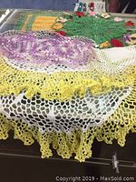 Overview of multiple crochet doilies layered, showing yellow, white, and purple with scalloped edges