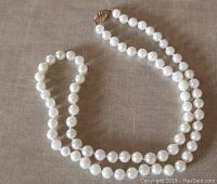 Full view of the pearl necklace laid out on fabric, showing overall length and bead uniformity
