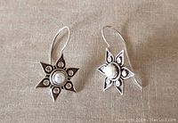 Pair of sterling silver star-shaped earrings with darkened detail and central white freshwater pearl on fabric background.