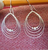 Front view close-up of both earrings showing teardrop shape formed by thin sterling silver wires with three small silver beads on innermost wire loop.